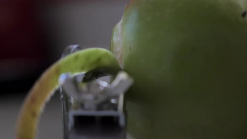 Slow motion side perspective metal kitchen device peeling, cutting and core green juicy apple skin o