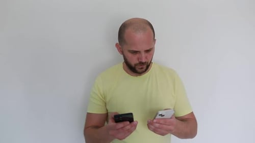 Man Comparing Two Smartphones in His Hands Against a Plain Background
