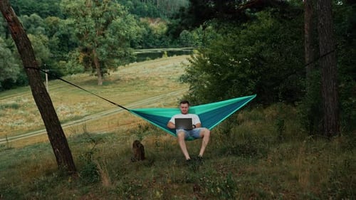 Man Working on Laptop in Hammock Outdoors