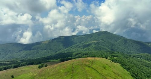 Flight over green mountain peaks. A beautiful sunny summer day at high altitude with thick clouds an