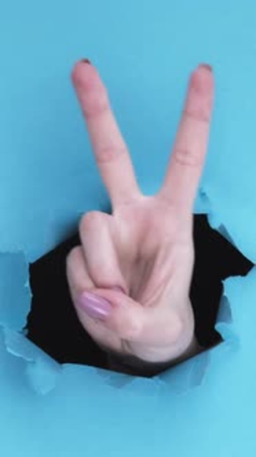 Hand Makes Peace Sign Through Blue Paper Hole