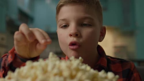 Blond Boy Enjoys Popcorn Snack Indoors, Close-up