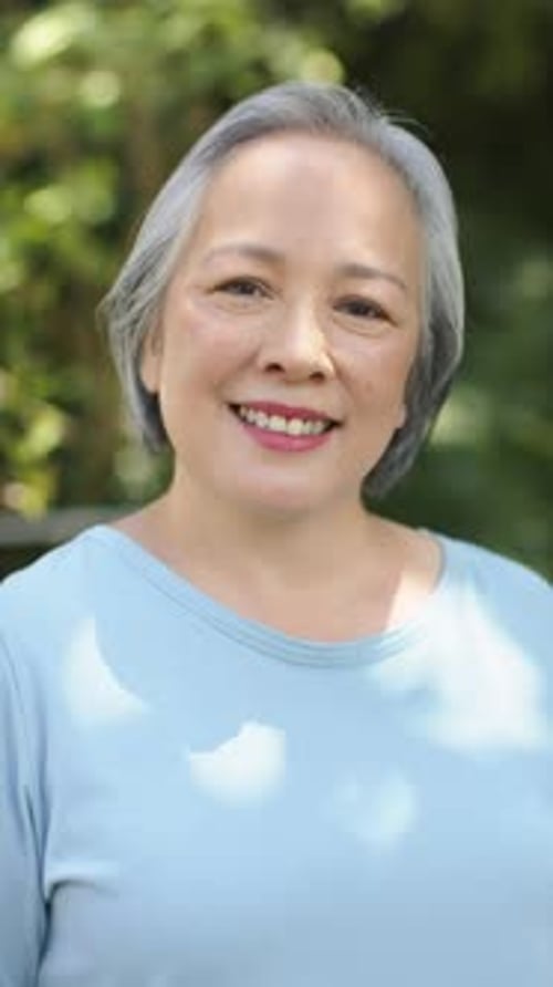 Vertical video: Smiling senior woman enjoying outdoor time in casual blue shirt