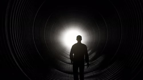 Silhouette of Man Walking Towards Light in Dark Tunnel