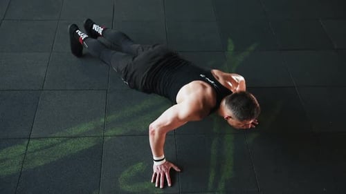Young sportive strong man in black wear doing push-ups in gym