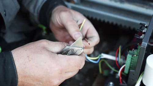 Man Strips Wires with Utility Knife on Electrical Panel
