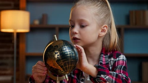 Süßes, cleveres kleines kaukasisches Kind, Kind, Mädchen, Tochter, dreht eine goldene Kugel und lernt abends zu Hause