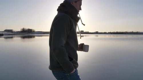 Follow shot of young male travel walking at scenic lake while drinking coffee