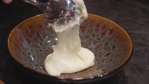 Chefs makes plating of meat and mashed potato dish, adding bits of green veggies nn top. Close up, s