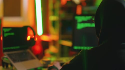 Hacker Writing Code Cracking Computer Man Programmer in Hoodie Cracks System Using Computer in Dark