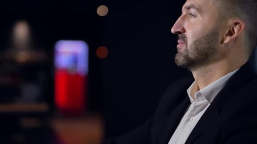 Nachdenklicher Mann in den Dreißigern, der im dunklen Raum sitzt.
