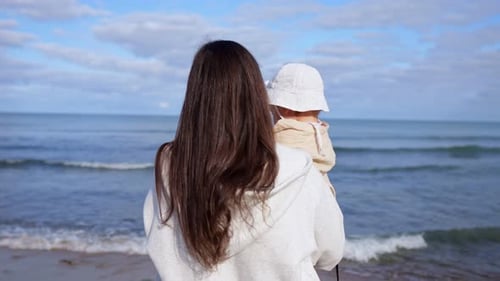 Mommy Carefully Holds Daughter in Arms Watching Sea Waves
