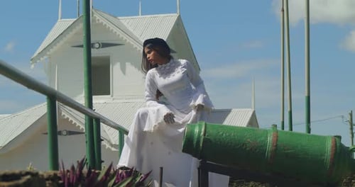 A child in a vintage wedding dress standing at the edge of a fort’s stone wall.