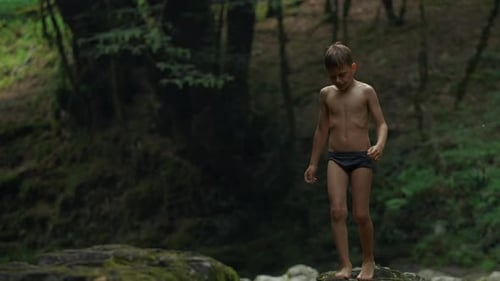 Menino descalço atravessando um rio frio de montanha