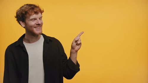 Smiling Man Pointing to Copy Space on Yellow Background