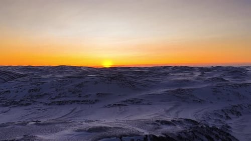 Aerial drone footage of sunset or sunrise in Norway mountains during winter time with orange sky.