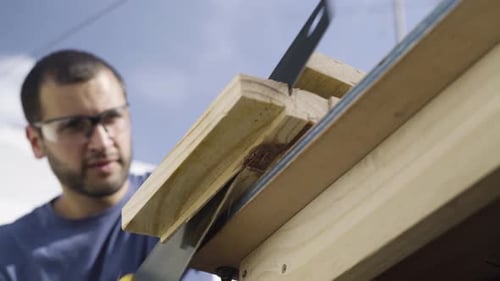 Man Sawing Wood on Workbench Outdoors