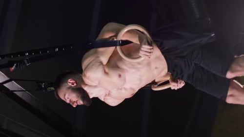 Vertical Video Male Gymnast is Working Out on a Rings in the Dark Gym