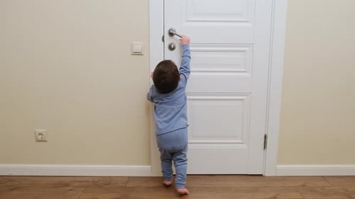 Little baby opens the door. Child pulls the door handle with the lock closed. Kid about two years ol