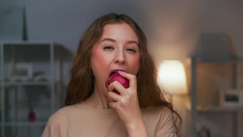Woman Bites Into a Red Apple Indoors