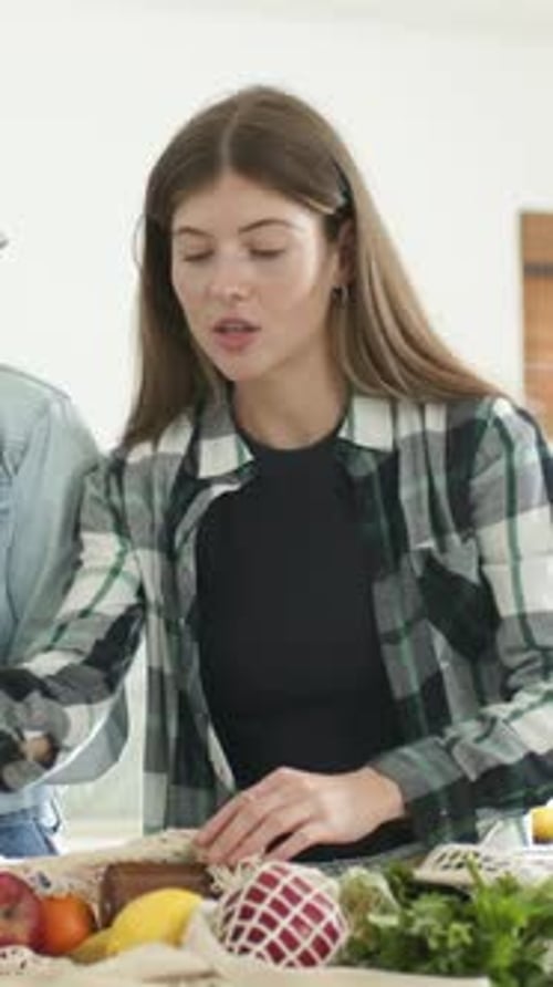 Vídeo vertical: Alcanzando a una mujer vestida a cuadros desempacando una bolsa de red en la cocina, comprobando la etiqueta del tarro ámbar