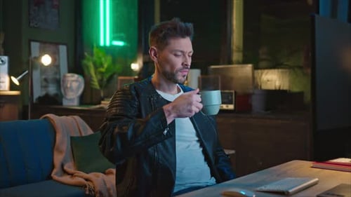 Man Working at Computer, Sipping Coffee at Night