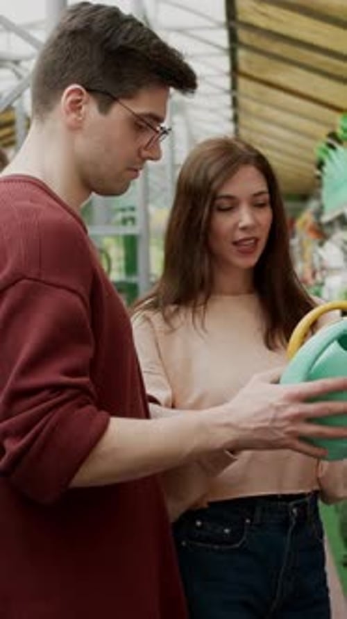 Focused Brunette Woman with Her Boyfriend Choosing the Color of a Watering Can in a Garden and
