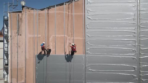 Zwei Bauarbeiter hängen an einer Fassade, während sie die alte Mauer reparieren