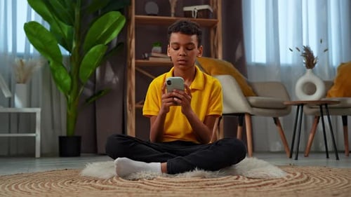 Teen Using Mobile Phone Sitting on Rug Indoors