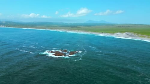 Stone formations above blue water surface and meadows in the distance