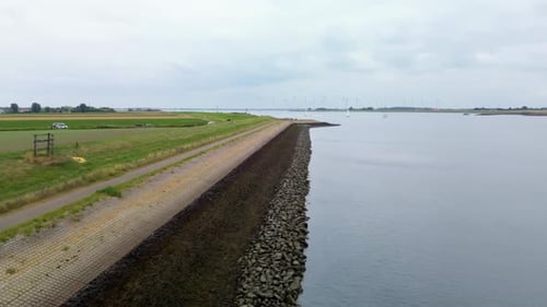 A calm coastal landscape with green fields, winding paths, and a seawall along the shore, captured