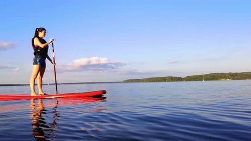 There is young girl paddle boarding in the big lake. she is alone there. in the other side of the la