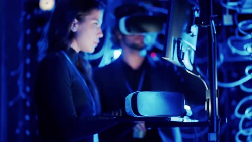 Woman programming in a server room while a man is using a Virtual Reality headset