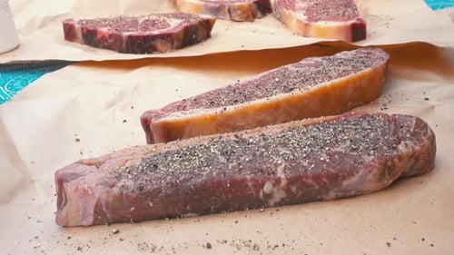slowmotion and close up of a man seasoning of raw beef and entrecote on a brown piece of paper