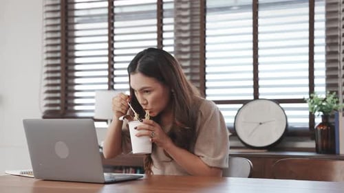 Woman Working at Desk with Computer and Noodles