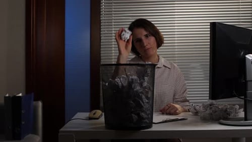 Woman Sitting at an Office Desk Looking Frustrated and Throwing a Crumpled Piece of Paper Into a