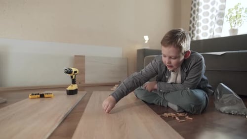 Weißer Junge sitzt in einer neuen Wohnung und hilft beim Zusammenbau der Möbel