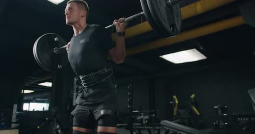 Bodybuilder with Athletic Body Doing Squat Exercise with Barbell in Gym