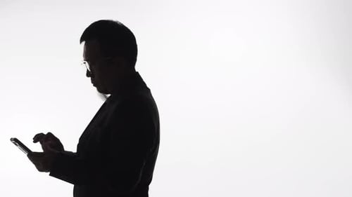 Silhouette of a man with a smartphone pacing back and forth as he works to solve a problem, send mes