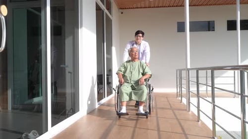 Doctor Pushes Senior Patient in Wheelchair at Hospital