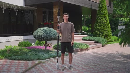 Um homem está em um jardim bem cuidado do lado de fora de um prédio moderno com um longo corta-sebes O