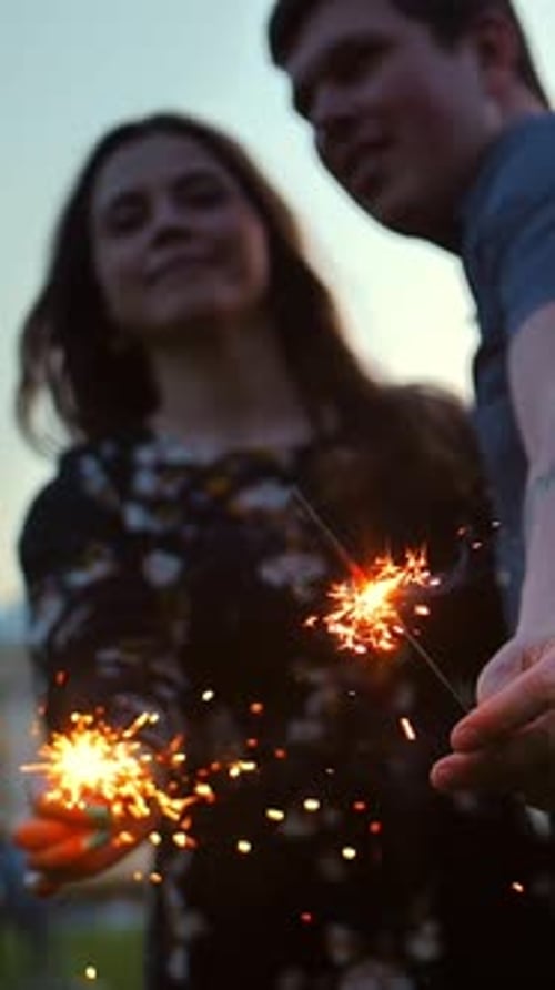 Happy Couple Holding Sparklers and Kissing Outdoors