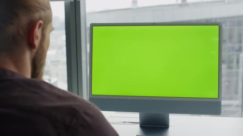 Mann liest alleine am Arbeitsplatz mit Blick auf die Stadt einen Mockup-Greenscreen-Computertext