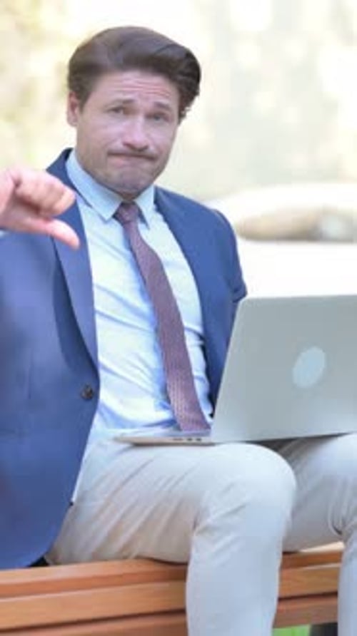 Thumbs Down by Businessman Working on Laptop Outdoor, vertical