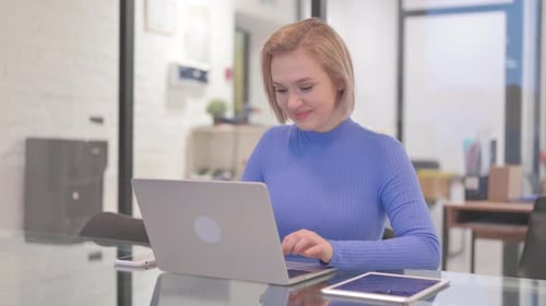 Young Woman Smiling at Camera while Working on Laptop in Office