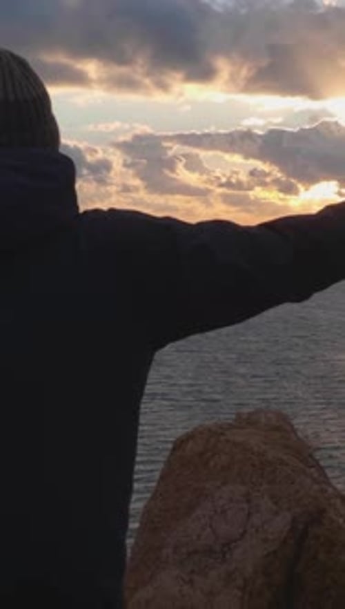 Person On Rocky Coastline at Sunset With Arms Up