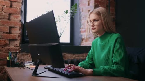 Frau tippt Text auf der Tastatur eines modernen Computers und arbeitet in einem modernen Büro mit Loft-Interieur