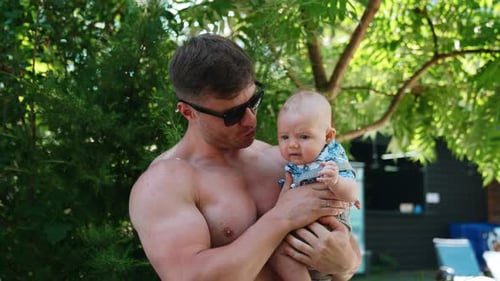 Shirtless Man Holding Baby in Green Backyard