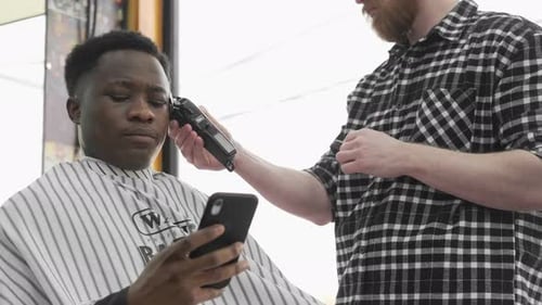 Man Gets Haircut at Modern Barbershop, Using Phone