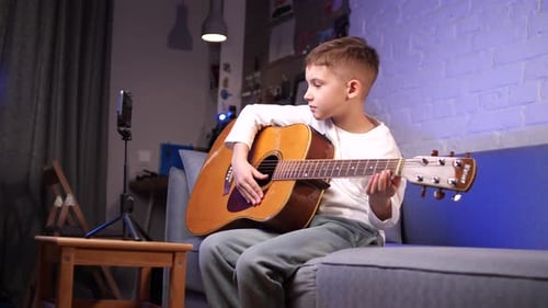 Young Boy Plays Guitar on Sofa at Home